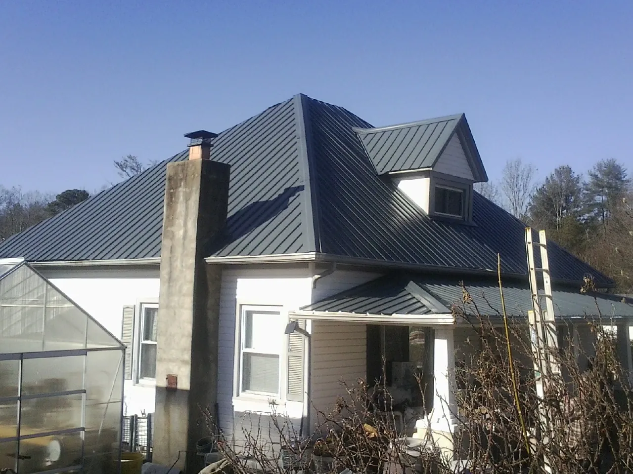 Dark blue standing seam metal roof on a white farmhouse with dormer — Slate & Tile Roof Repair by Roofing Brothers in Delong