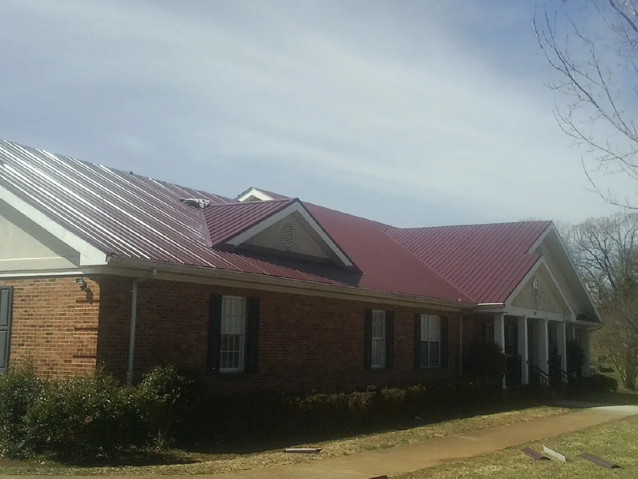 Red metal roof with gabled entries on a long brick building, from a Hail Damage Roof Repair job in Delong