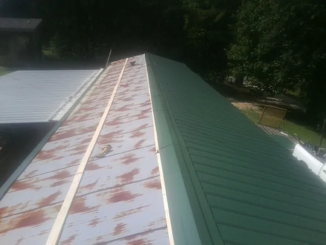 Old rusted panels beside newly installed green metal roofing — Wind Damage Roof Repair by Roofing Brothers in Delong