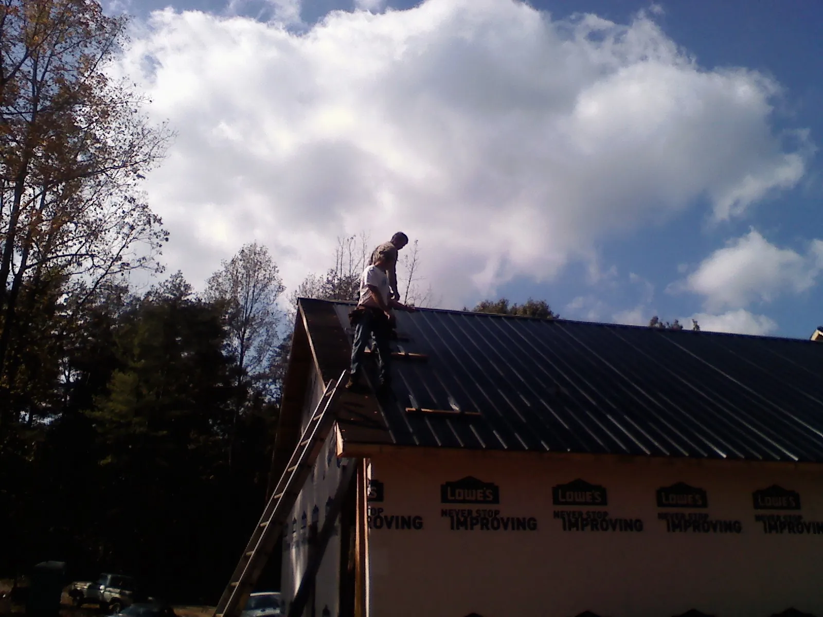 Roofer fastening dark metal panels high against a cloudy sky, from a Roof Inspection job in Delong