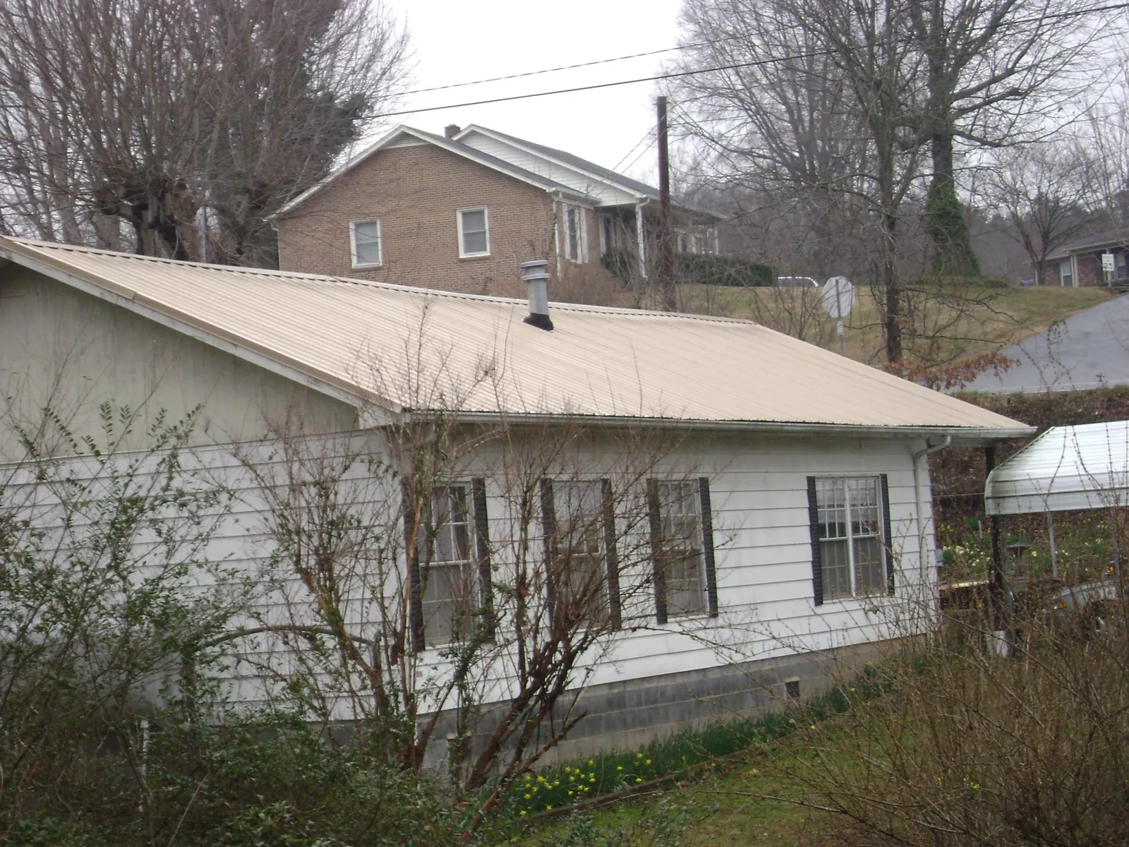 Tan metal roof on a white sided house set into a hillside — Commercial Roofing by Roofing Brothers in Delong