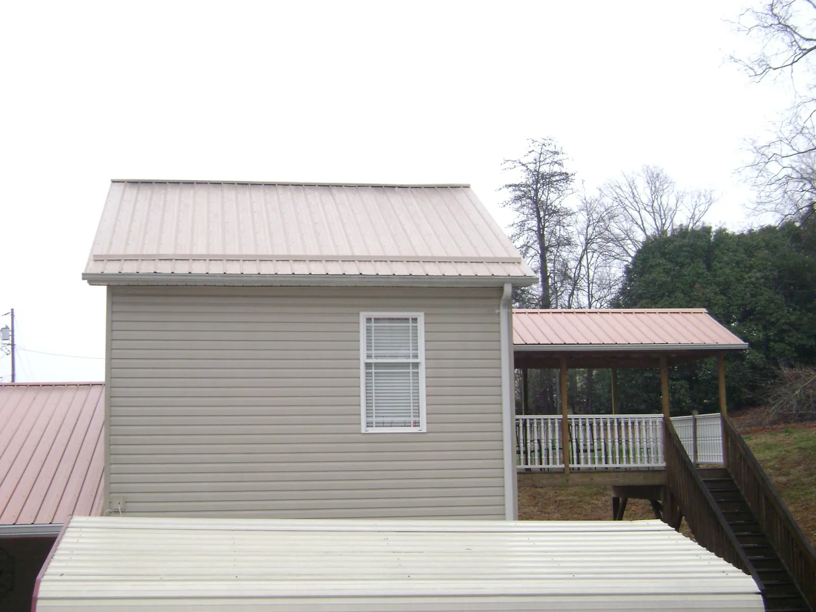 Tan metal roofs on a two story addition and attached porch, from a Roof Replacement job in Delong